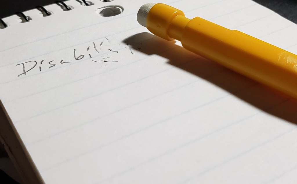 A pad of paper with the last few letters of "Disability" erased. A yellow mechanical pencil lies on the paper.